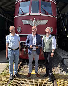 Wolfgang Ihrlich (Museumsleiter DB Museum Koblenz), Rainer Landwehr (CEO PIKO Spielwaren GmbH) und Matthias Fröhlich (Produktmanager PIKO Spielwaren GmbH) mit dem PIKO H0-Modell der Baureihe 119 vor der Museumslokomotive E 19 12 im DB Museum; Quelle: PIKO Spielwaren GmbH