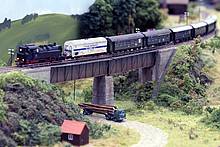 Die Dampflok der Baureihe 64 zieht einen Personenzug mit Güterbeförderung. Der Kühlwagen ist vorschriftsgemäß direkt hinter der Lokomotive in den Zug eingestellt.